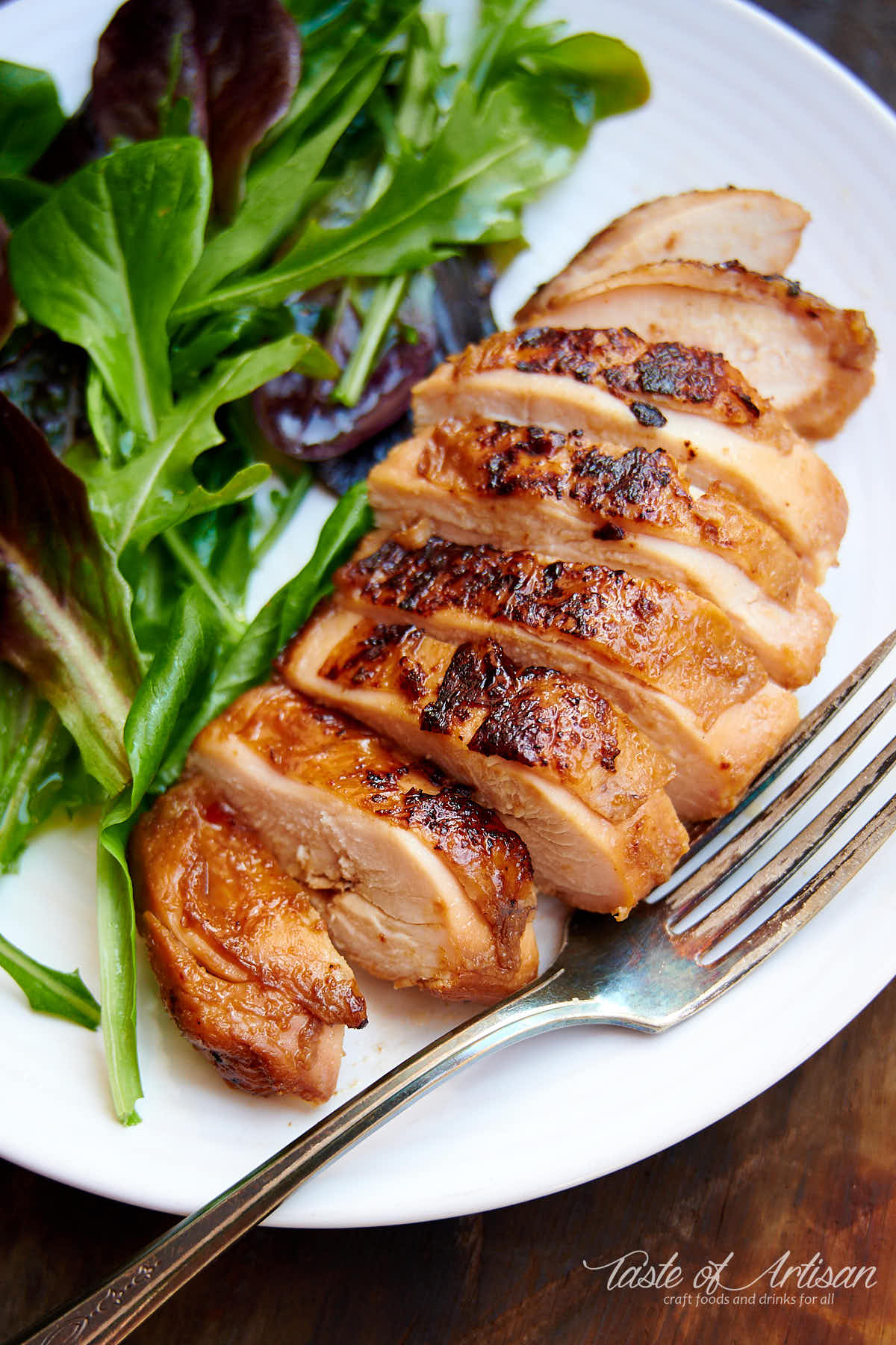 Sliced chicken breast, cooked sous vide, on a white plate with leafy greens on the side.