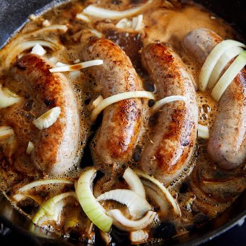 German bratwurst frying with onions in a cast-iron pan.