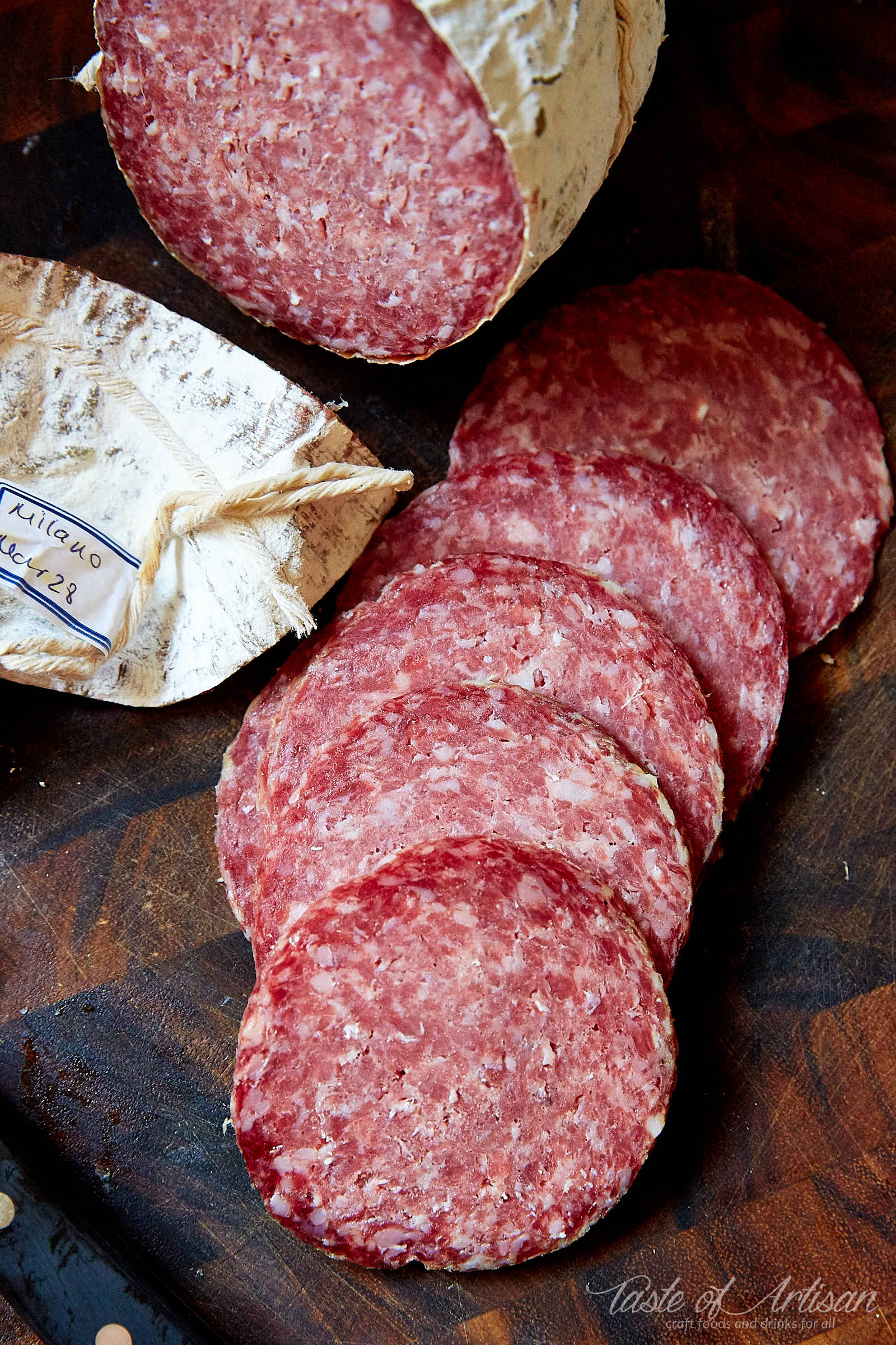 Homemade Milano Salami sliced on a brown board.