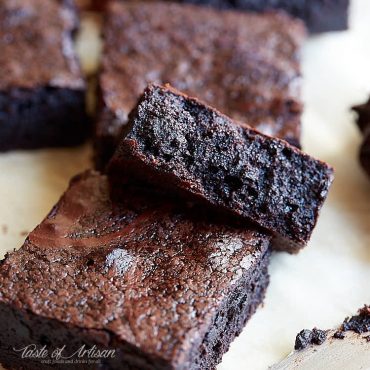 Flourless brownies cut into pieces on parchment paper.