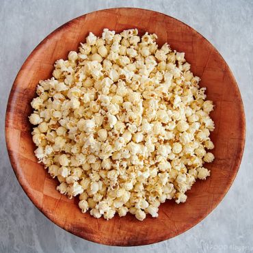 A large bamboo bowl filled with popped popcorn.