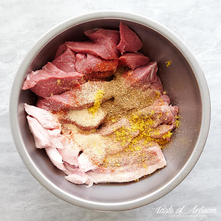 Cut up meat with spices for bockwurst sausage in a stainless steel bowl.