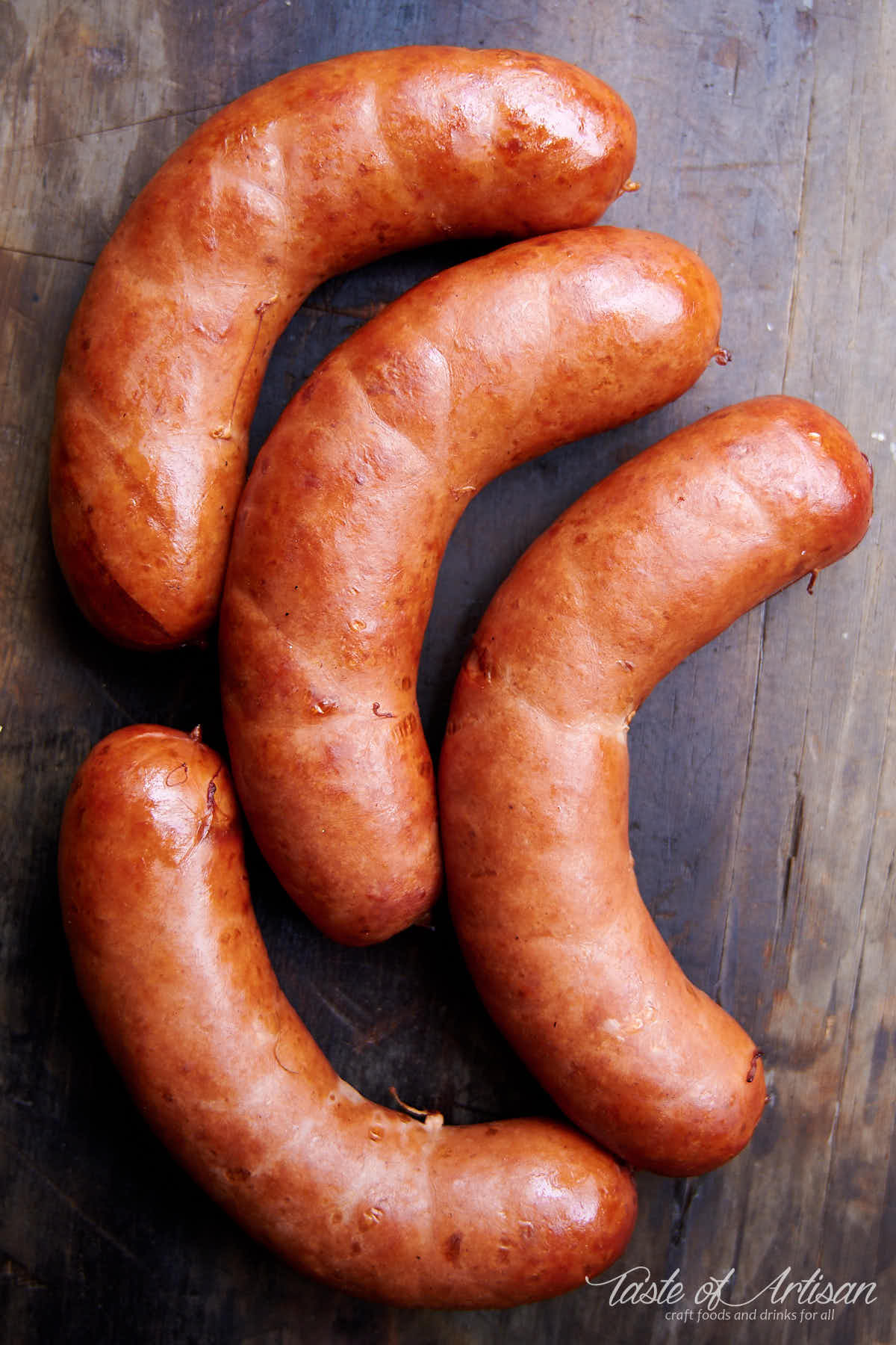 Top down view of four links of smoked bockwurst sausage on a brown board.