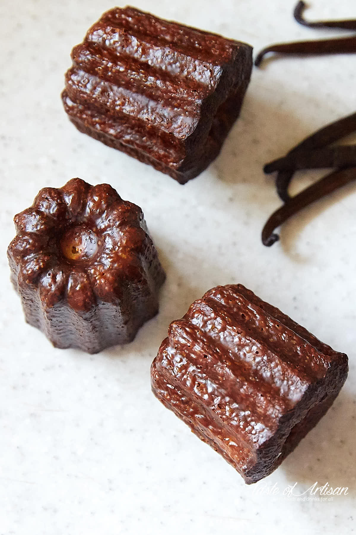 Caneles and vanilla beans on a white table top.