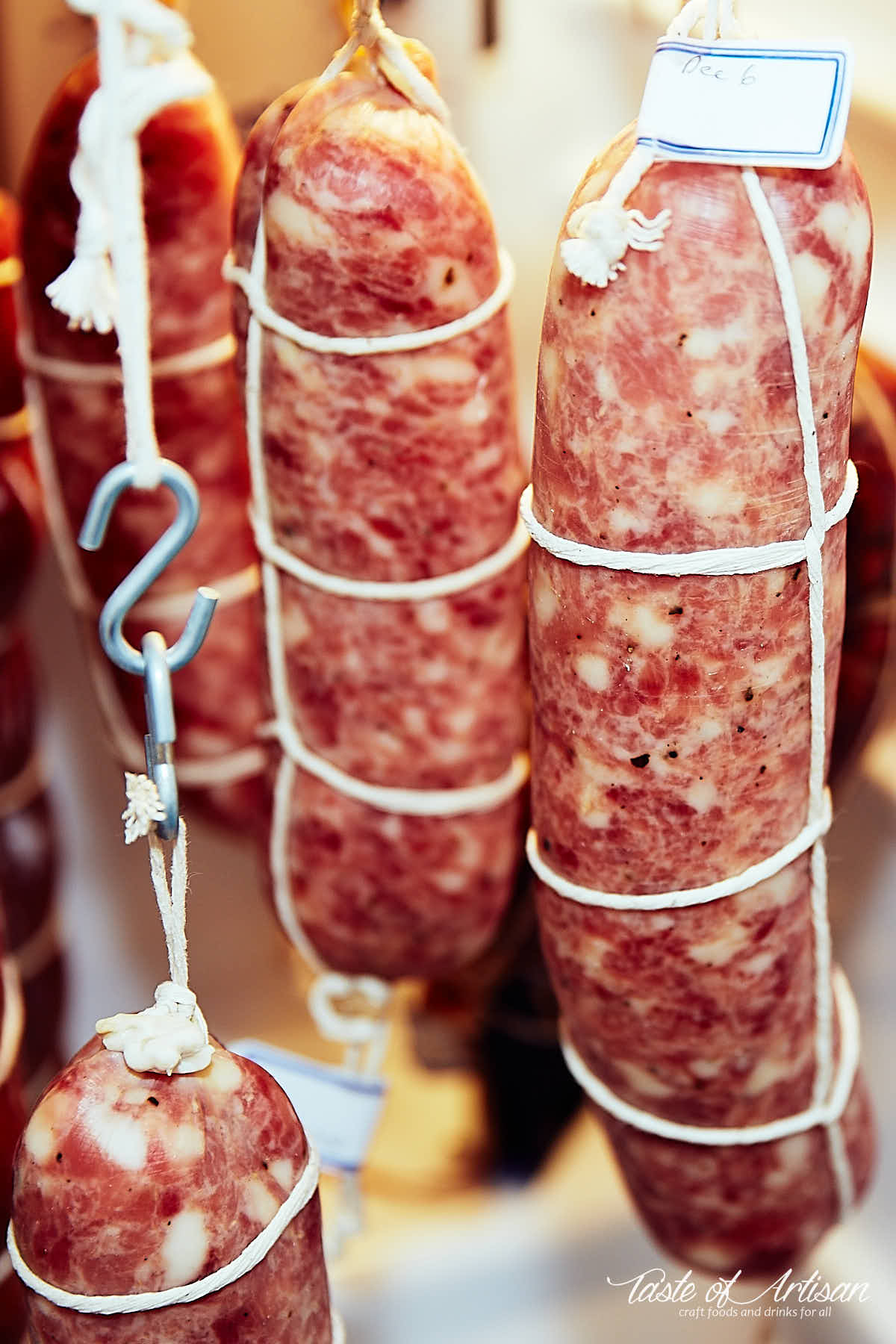 Soppressata, tied with twine, hanging in a meat curing fridge.