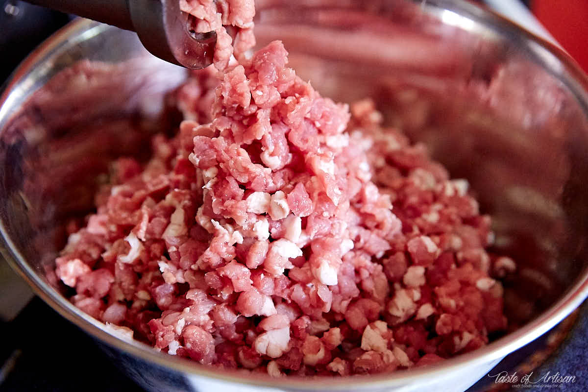 Ground pork falling in a bowl from Lem Meat Grinder for making sopressata.