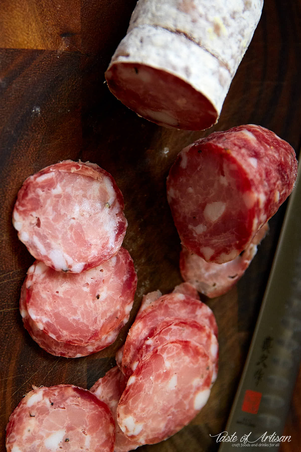 Slices of sopressata and knife on a cutting board.