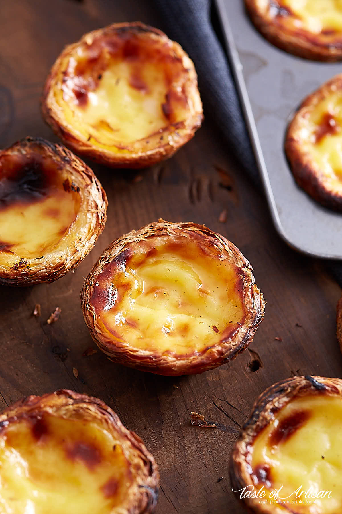 A view at an angle of custard tarts scattered on a brown board.
