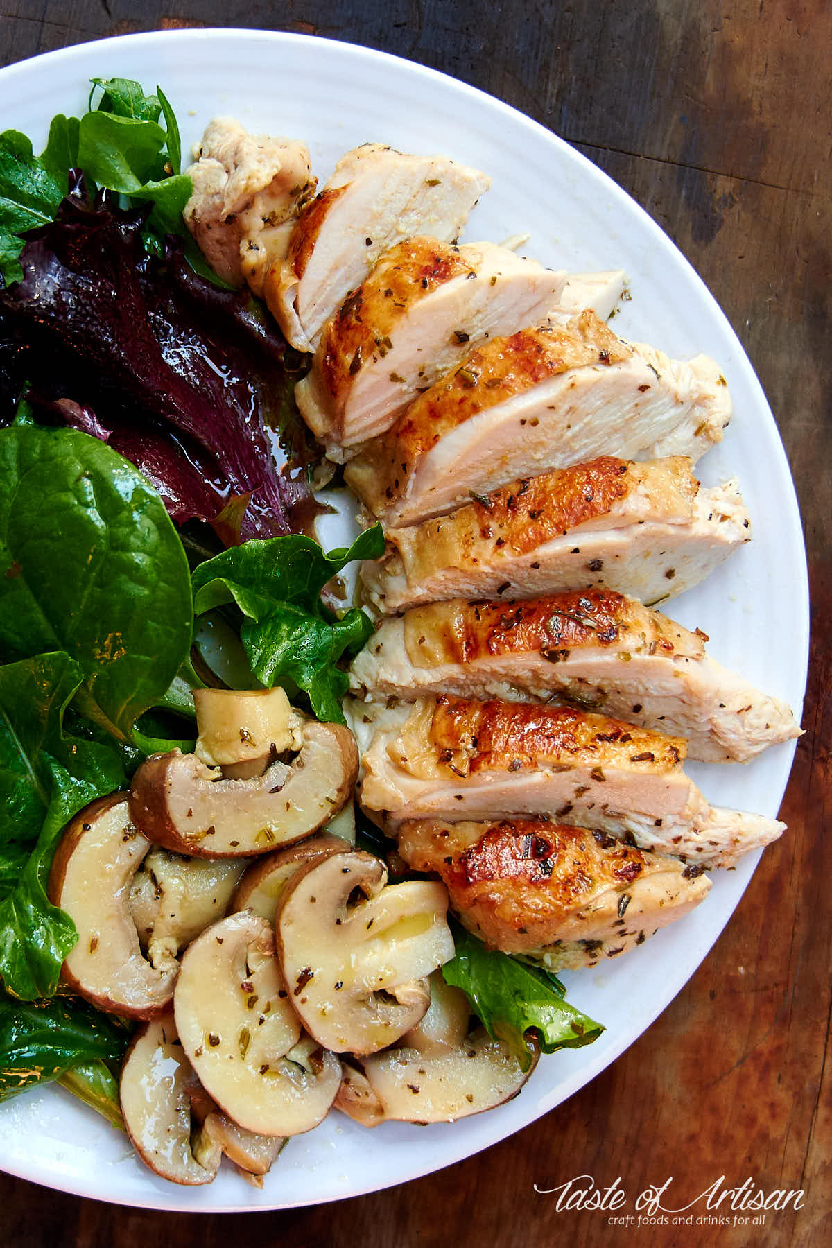 Top down view of sous vide chicken on a white plate with garden greens.