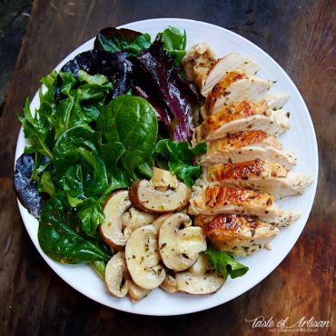 Sous vide chicken breast on a white plate with mushrooms and salad.