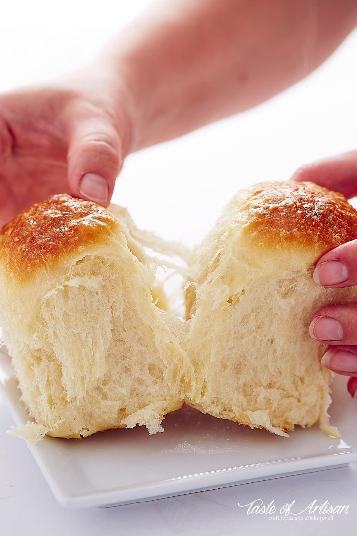 Two hands pulling two yeast rolls apart, flaky dough visible.