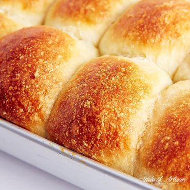 View at an angle of golden tops of yeast rolls in a baking pan.