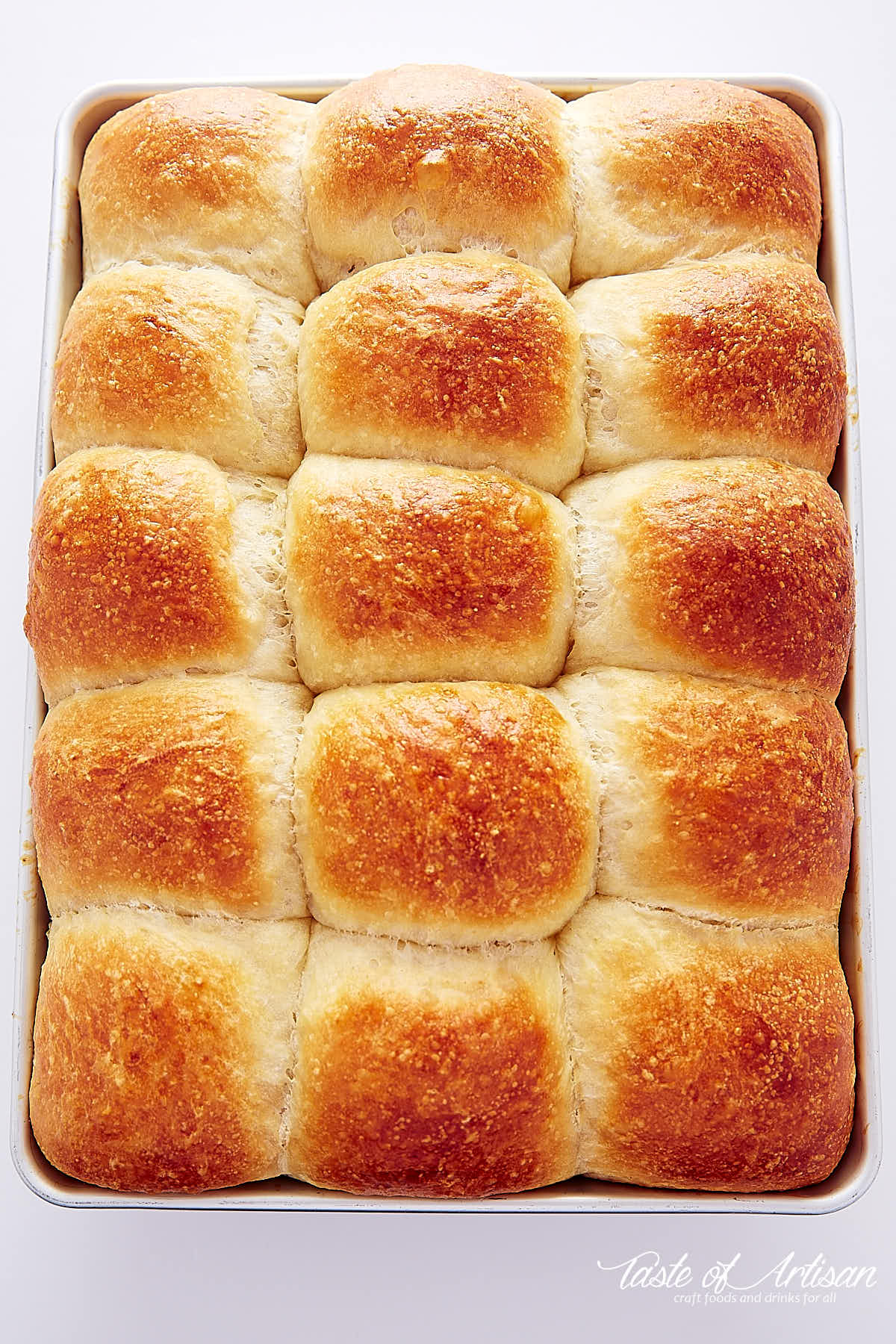 A top down view of a baking pan full of golden brown topped yeast rolls in a baking pan.
