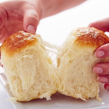 Two hands pulling two yeast rolls apart, flaky dough visible.