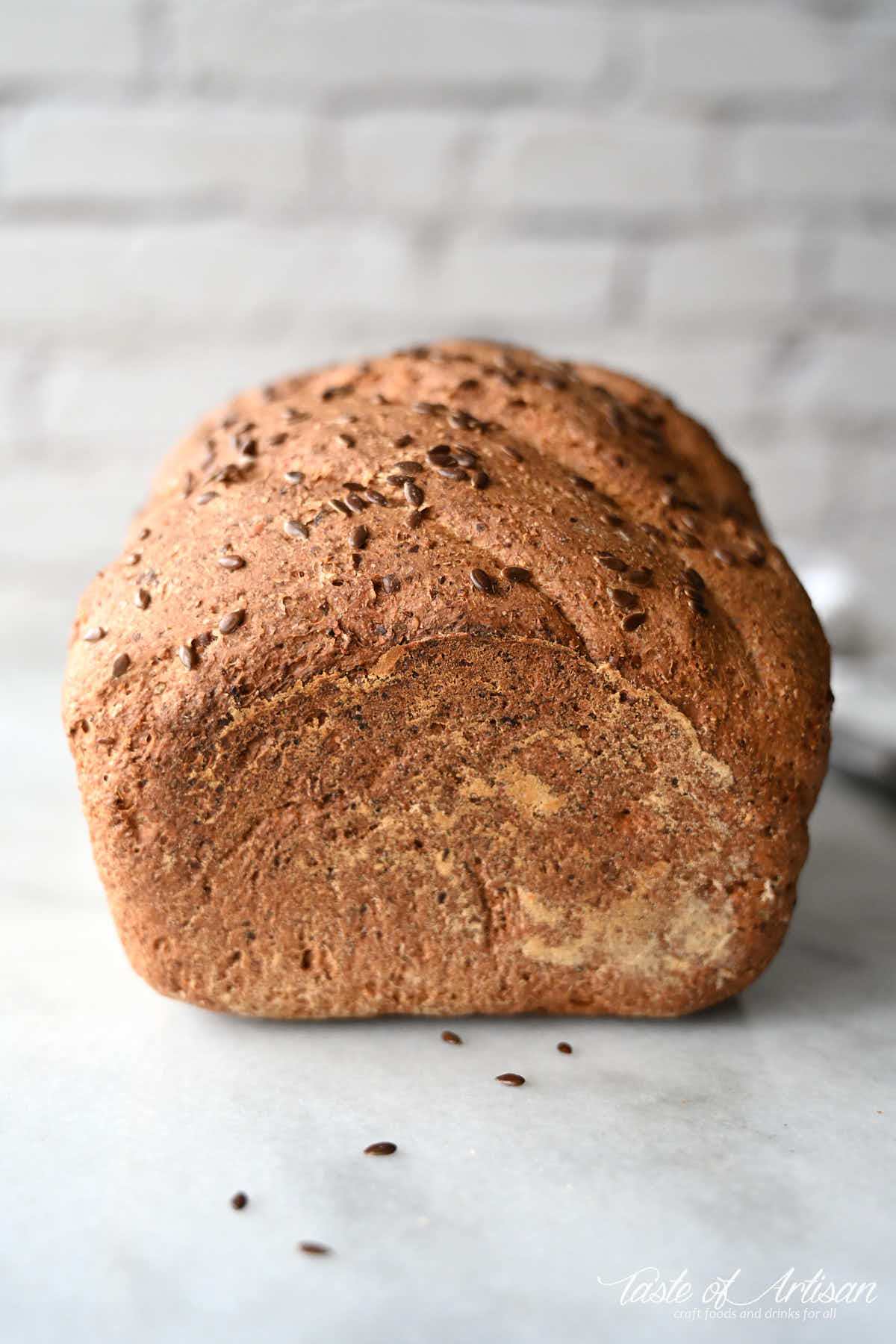 A loaf of flaxseed bread on a white marble board.