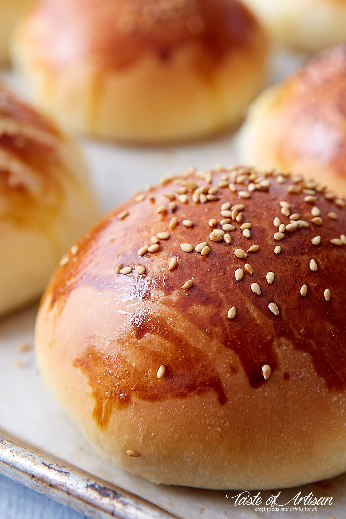 A close up of golden brown brioche bun with sesame seeds on top.