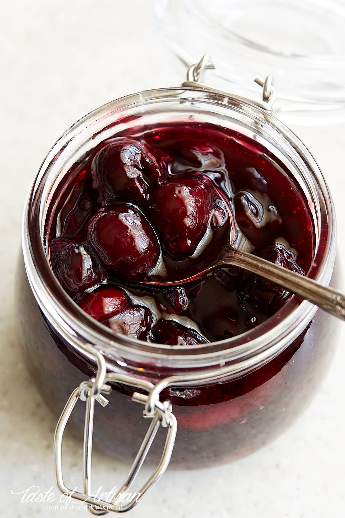 Cherry pie filling inside a jar with a spoon inserted in the jar.