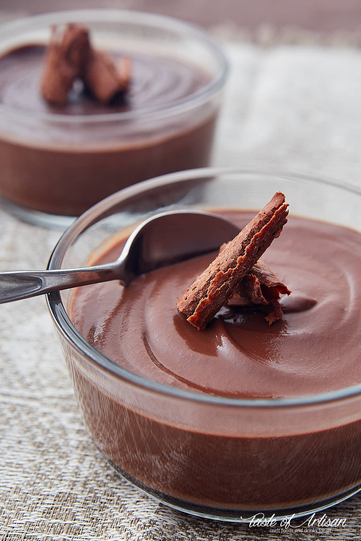 Chocolate pudding in a container with a spoon and shaved chocolate on top.