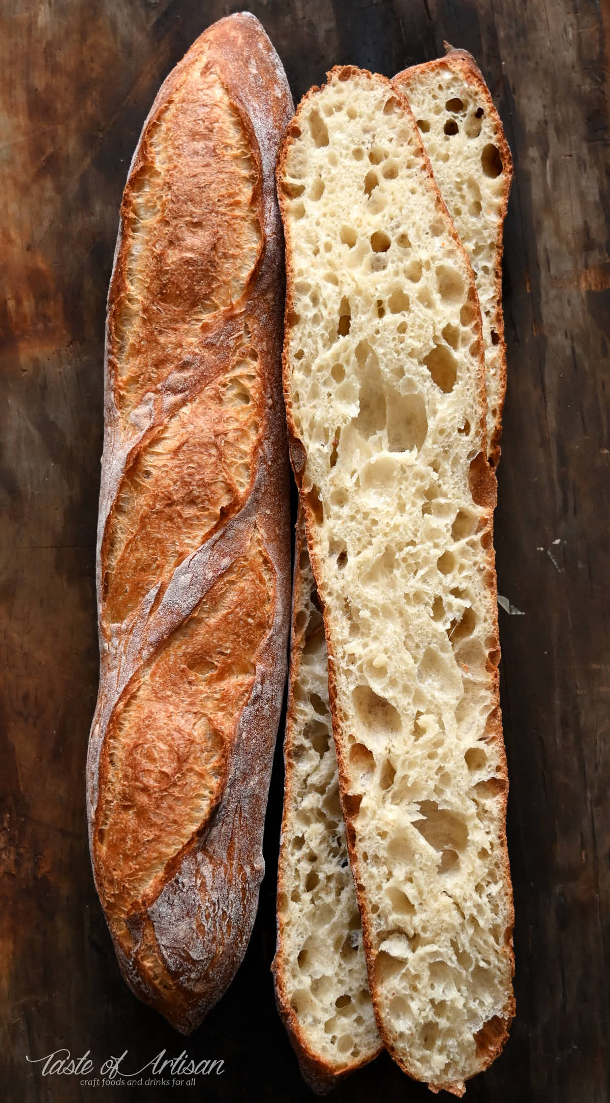 Two homemade French baguettes on a baking sheet, one cut open in half showing airy crumb.