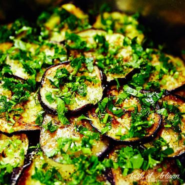Close up of marinated eggplant slices sprinkled with chopped greens.