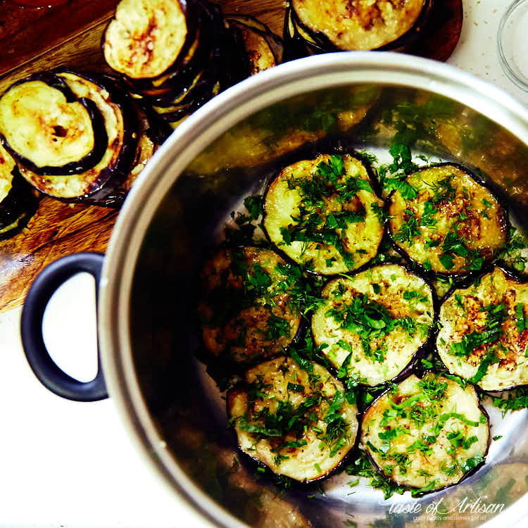 Layering eggplant slices and chopped greens in a pot.