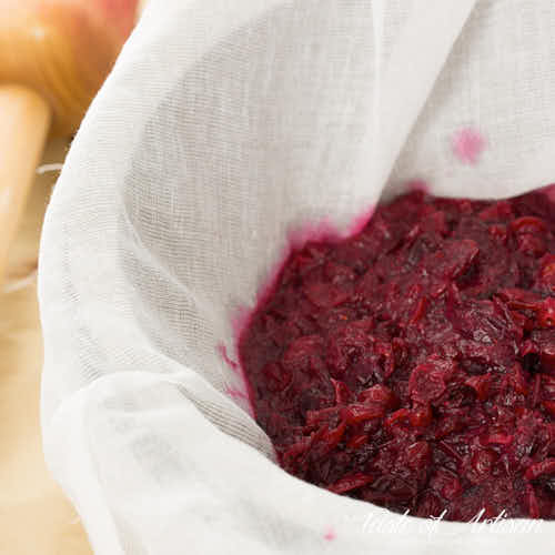 Smashed cranberries inside a colander lined with cheesecloth.