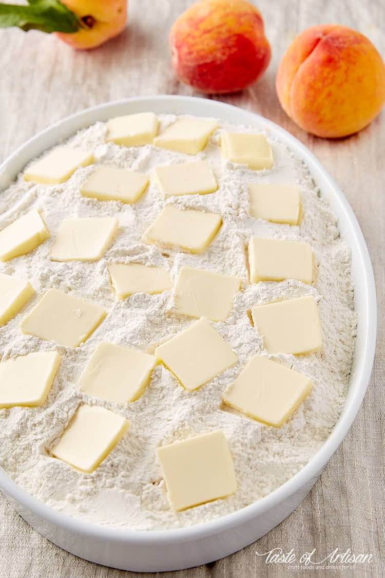 Raw peach dump cake in a baking dish, dry flour with butter pats on top.