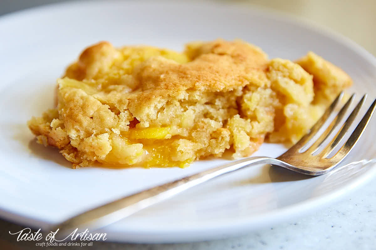 S slice of peach dump cake on a white plate with a fork.