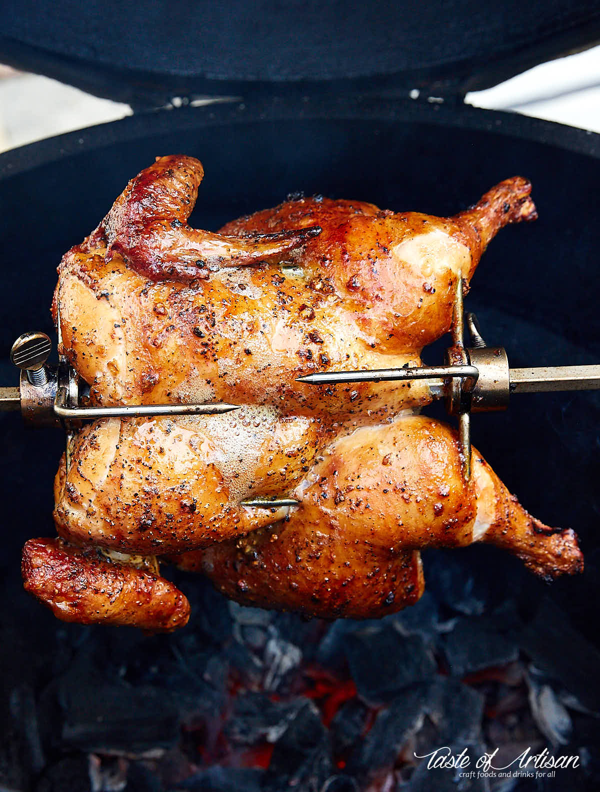 Crispy, browned chicken cooking on a rotisserie over hot charcoals.