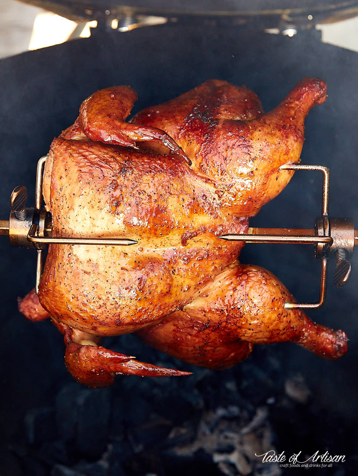 Crispy, browned chicken cooking on a rotisserie over hot charcoals.