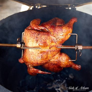 Crispy, browned chicken cooking on a rotisserie over hot charcoals.
