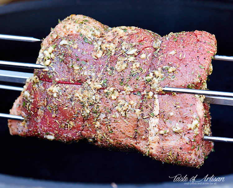Raw top round roast, crusted with garlic and herbs on a rotisserie spit.