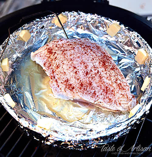 Raw turkey breast inside a smoker in a foil pan.