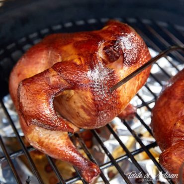 Whole chicken, nicely browned, sitting on rack inside a smoker.
