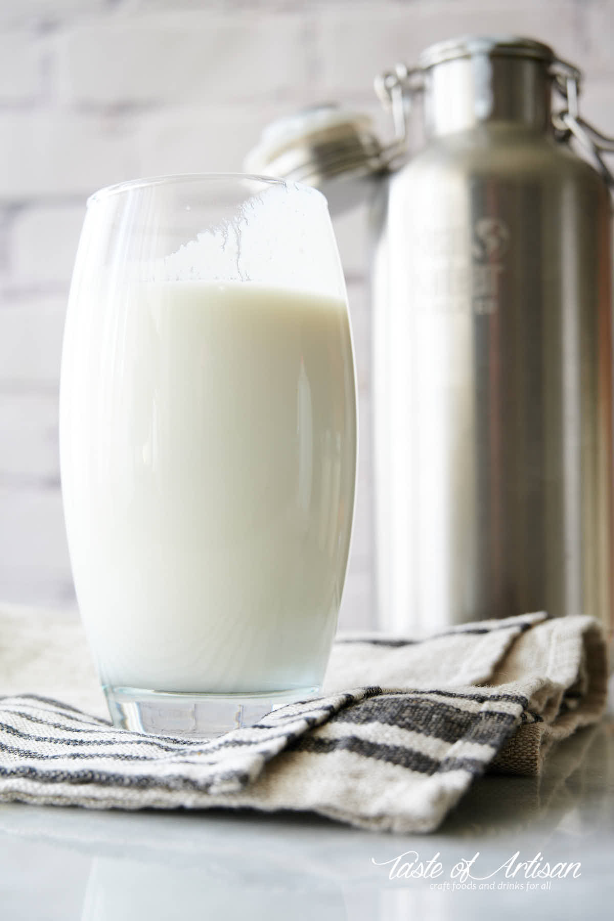 A glass of buttermilk on a table, thermos on the background.