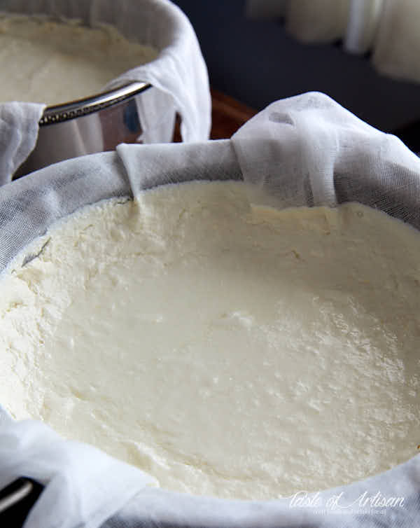 Two colanders lined with muslin with draining curd inside.