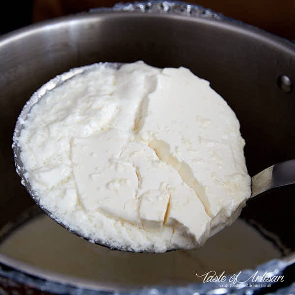 Ladling curd from the pot into a draining bowl.