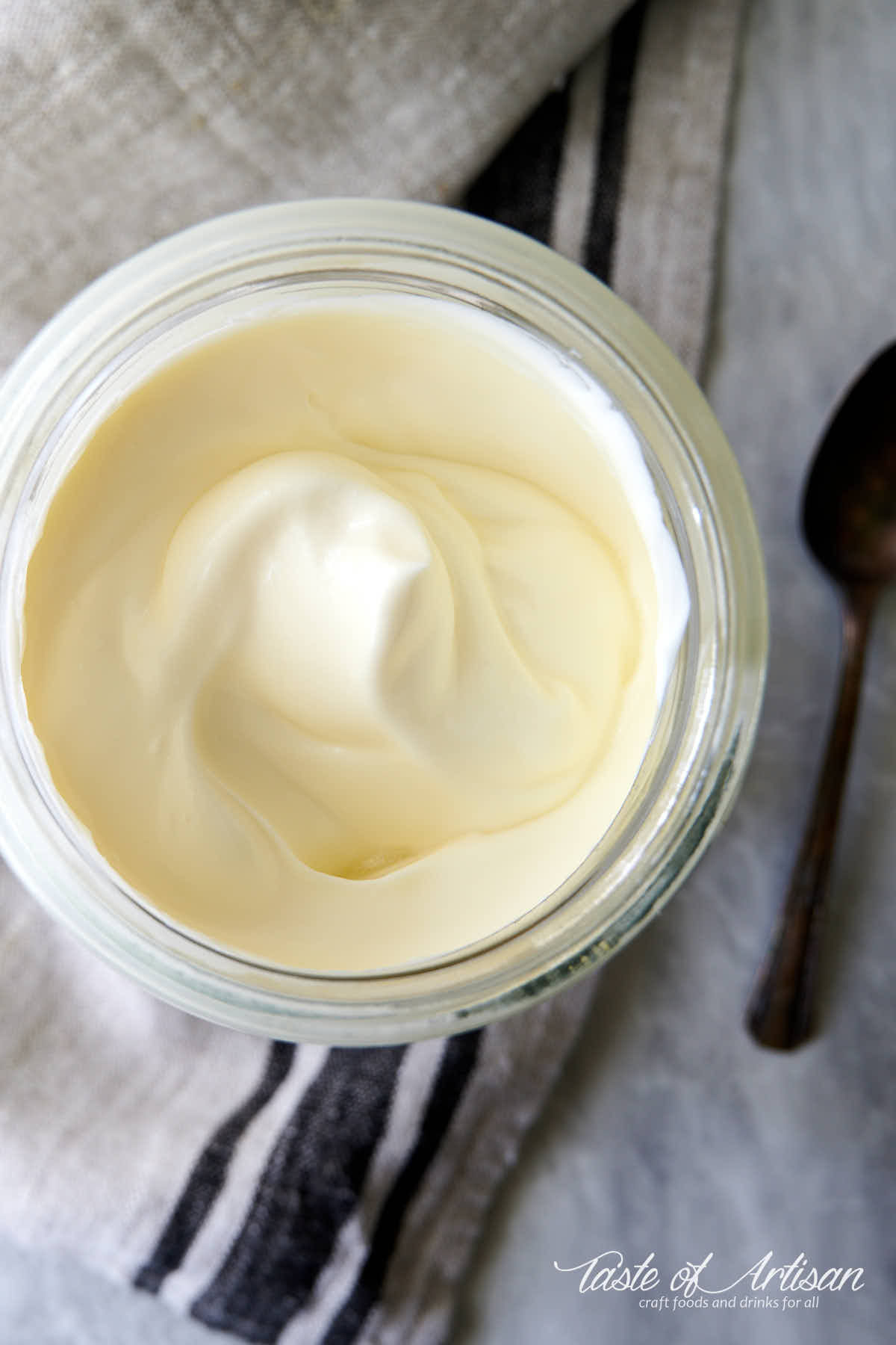 Creme fraiche in a 1 qt jar on a towel with a spoon next to it.