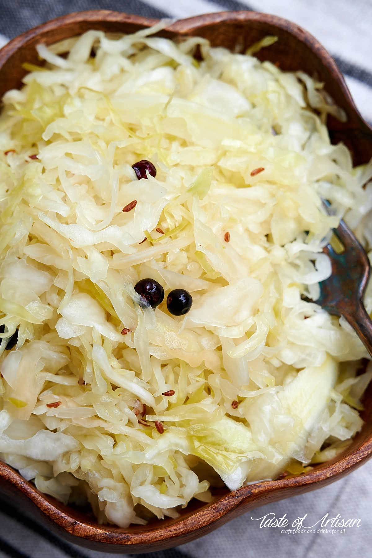 Top down view of a brown wooden bowl with homemade sauerkraut and a fork.