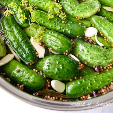 Close up of whole pickles in pickling juice in a pot.