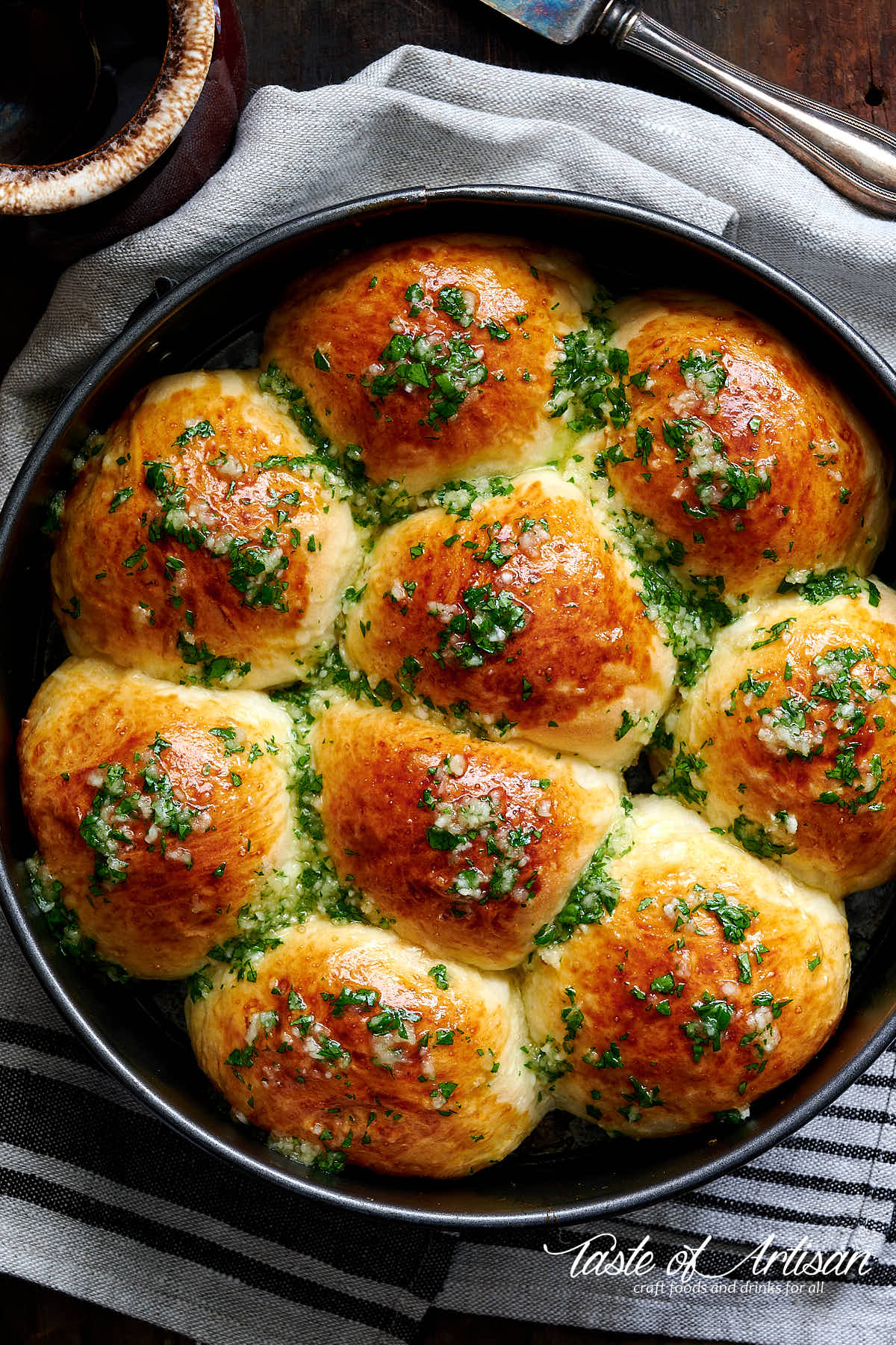 Top down view of pampushki in cake pan drizzled with garlic sauce and chopped greens.