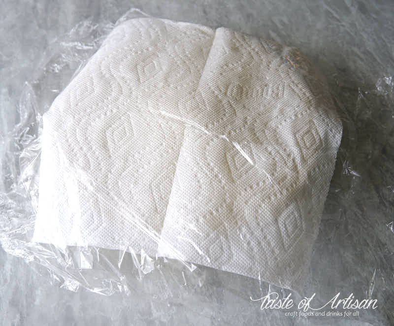 Bread covered with a paper towel and plastic.