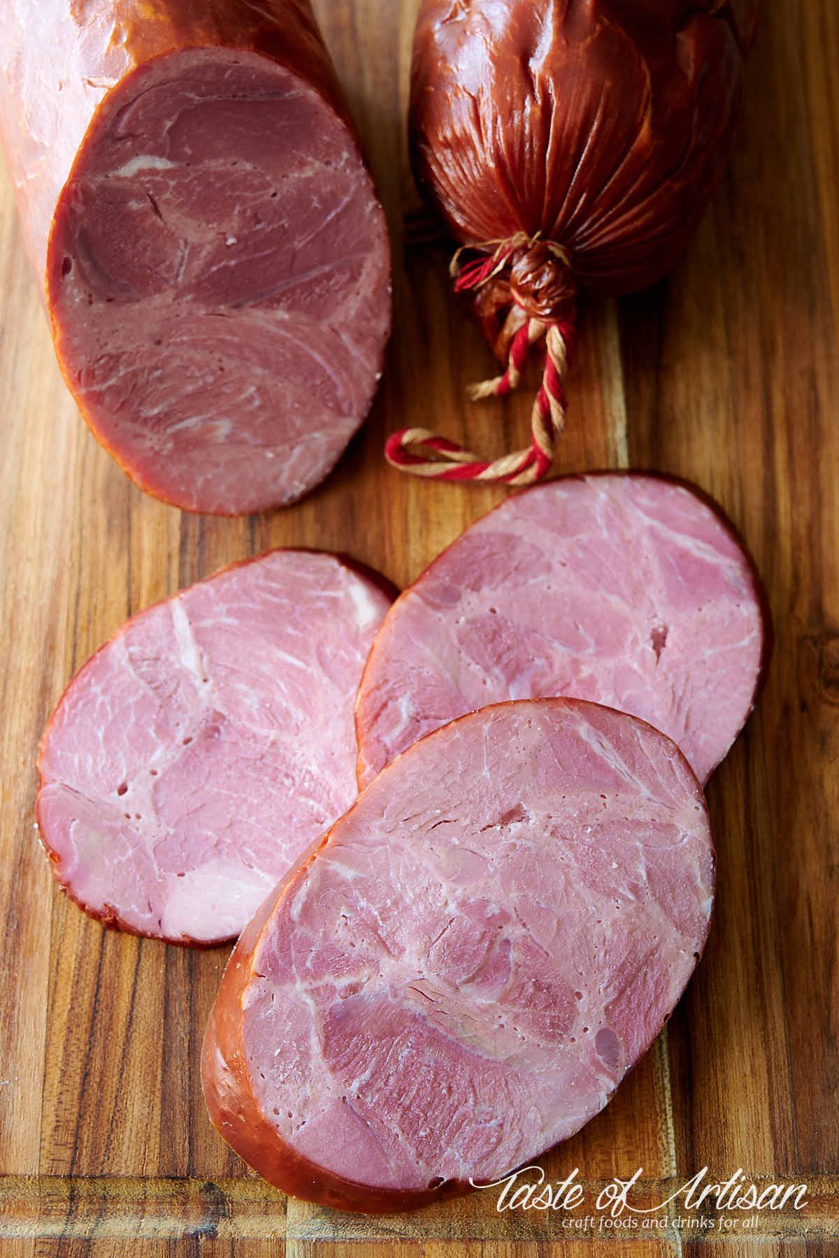 Slices of krakow sausage on a brown cutting board. A larger krakow sausage on background.