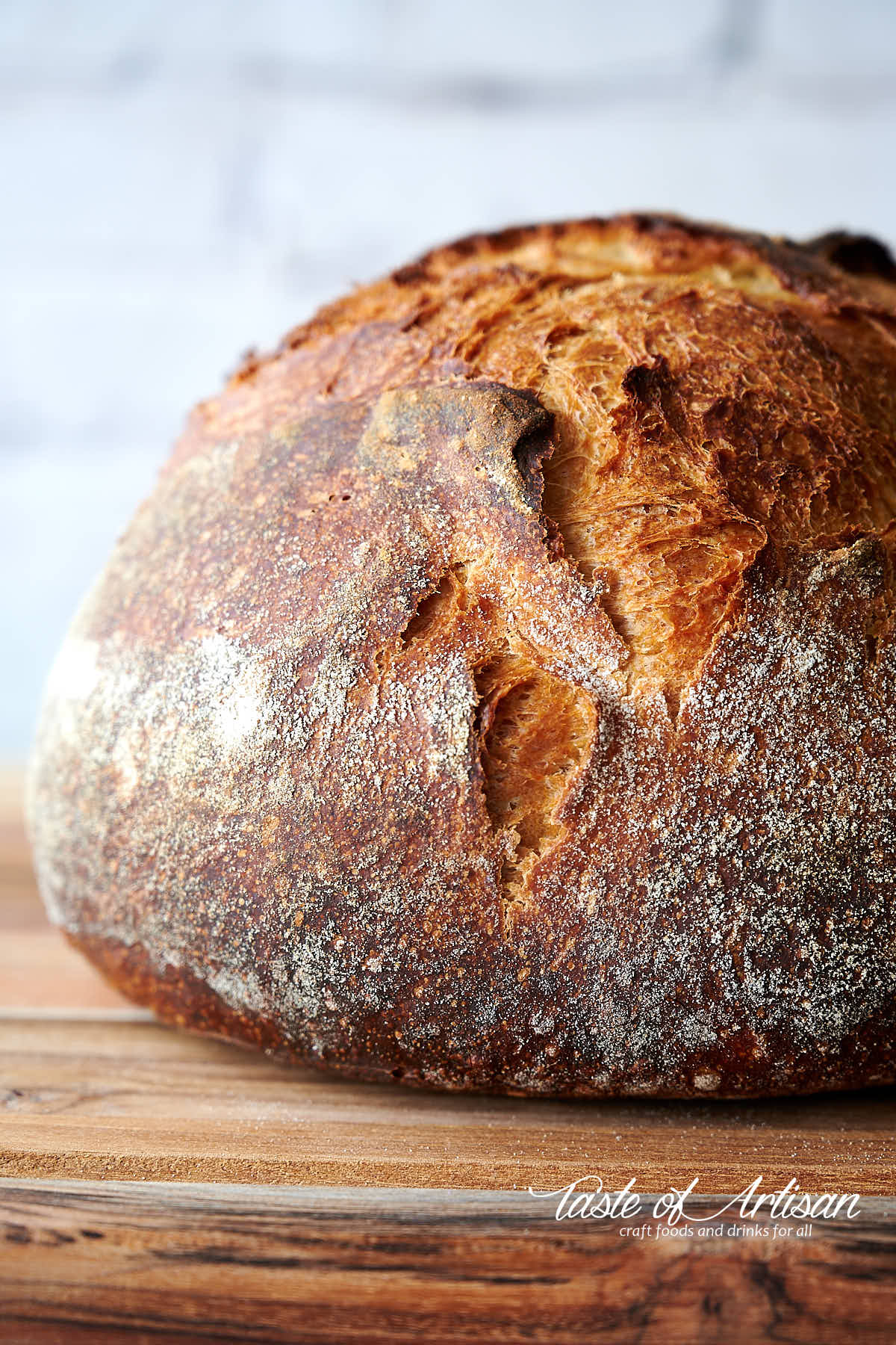 A loaf of no-knead bread on a brown wooden cutting bread. Beautiful dark brown crust.