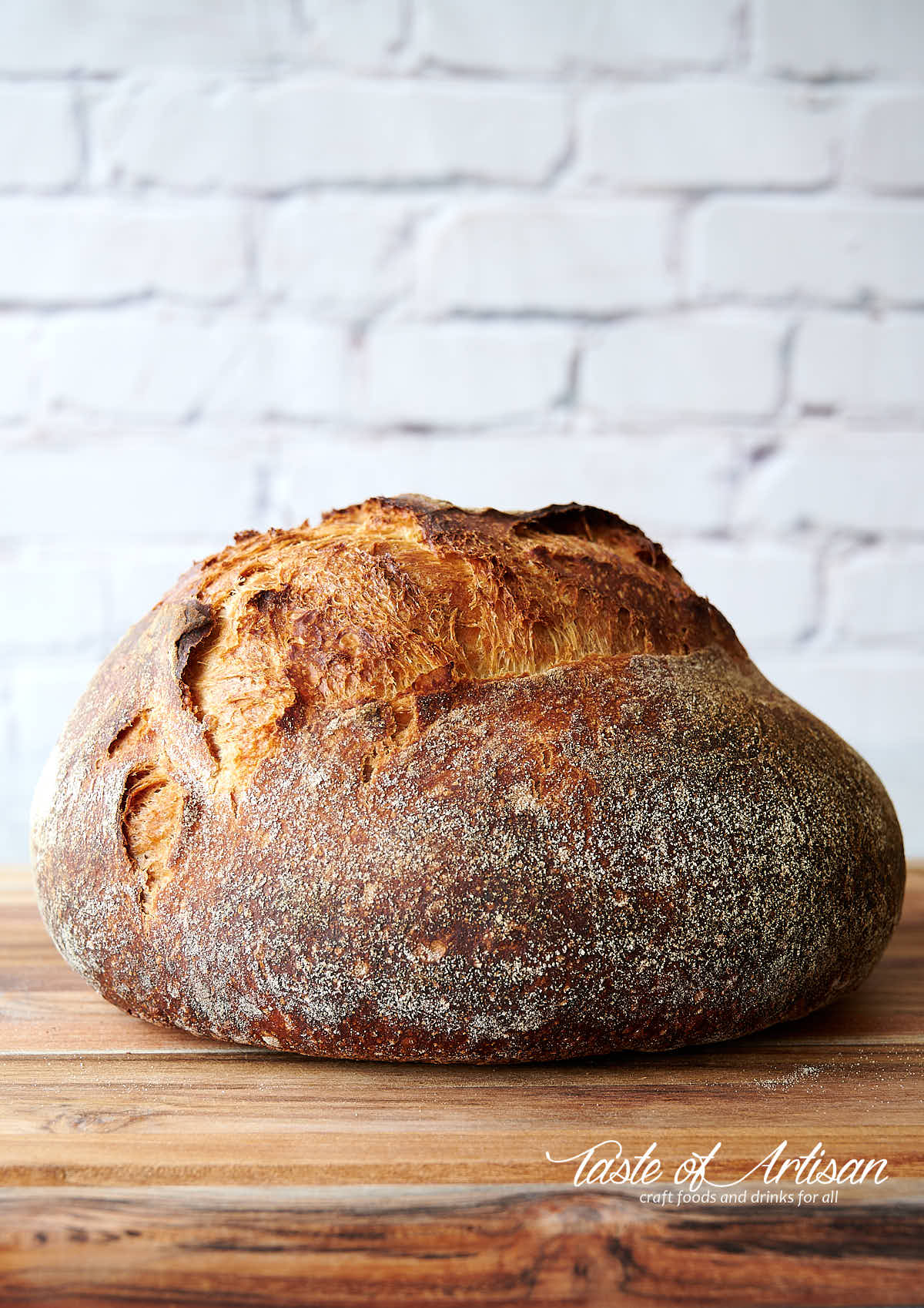 Golden brown loaf of no knead bread on a light brown cutting board.