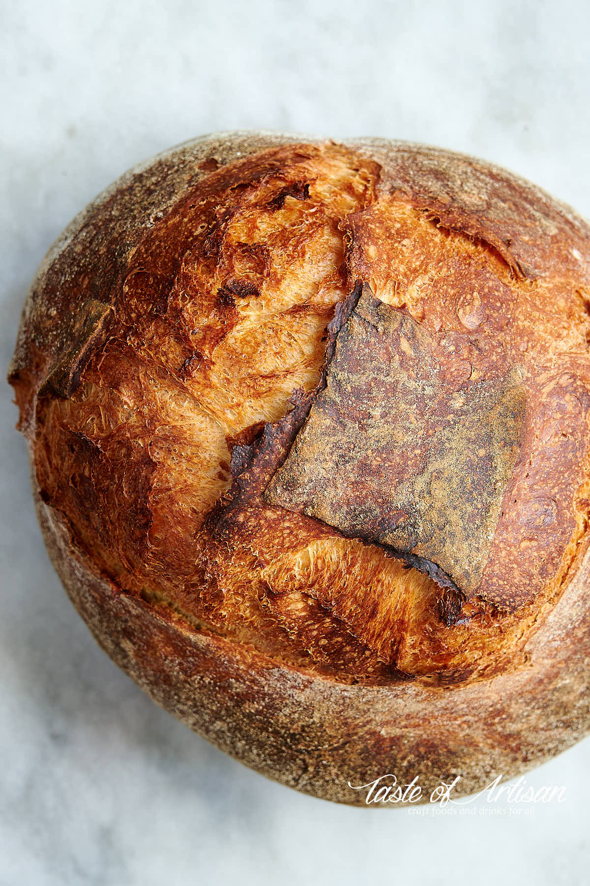 Top down view of golden brown, crusty bread loaf on a white marble board.