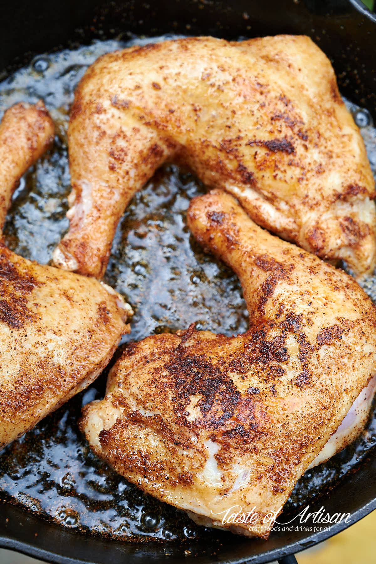 Chicken leg quarters frying on cast iron pan.