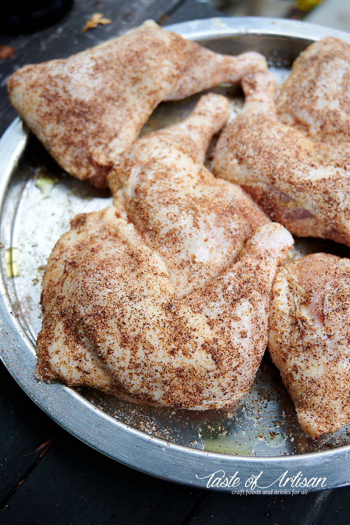 Raw chicken leg quarters sprinkled with seasonings.