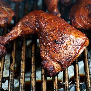 Smoked chicken leg quarter on the grate of a smoker.