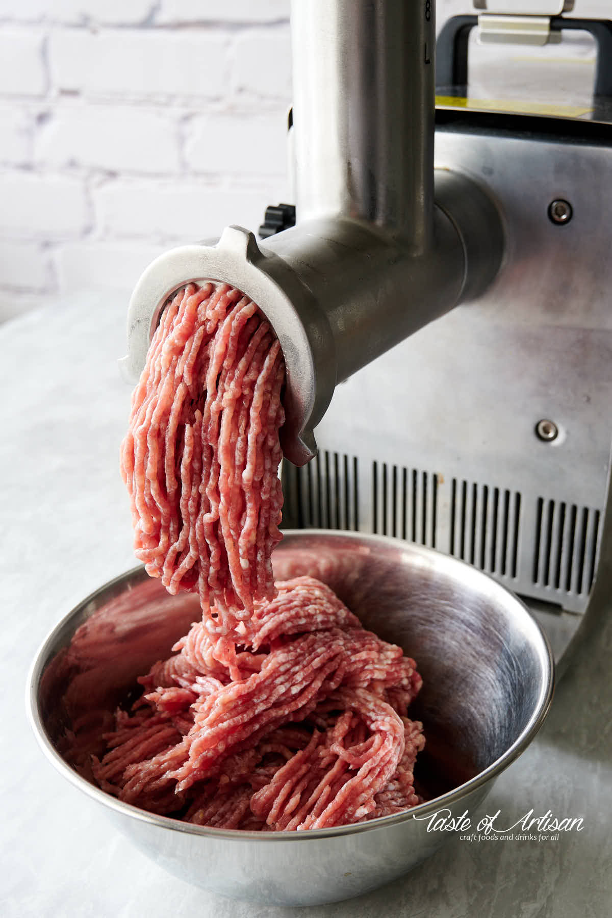 Ground meat coming out of meat grinder and falling in a stainless bowl. 